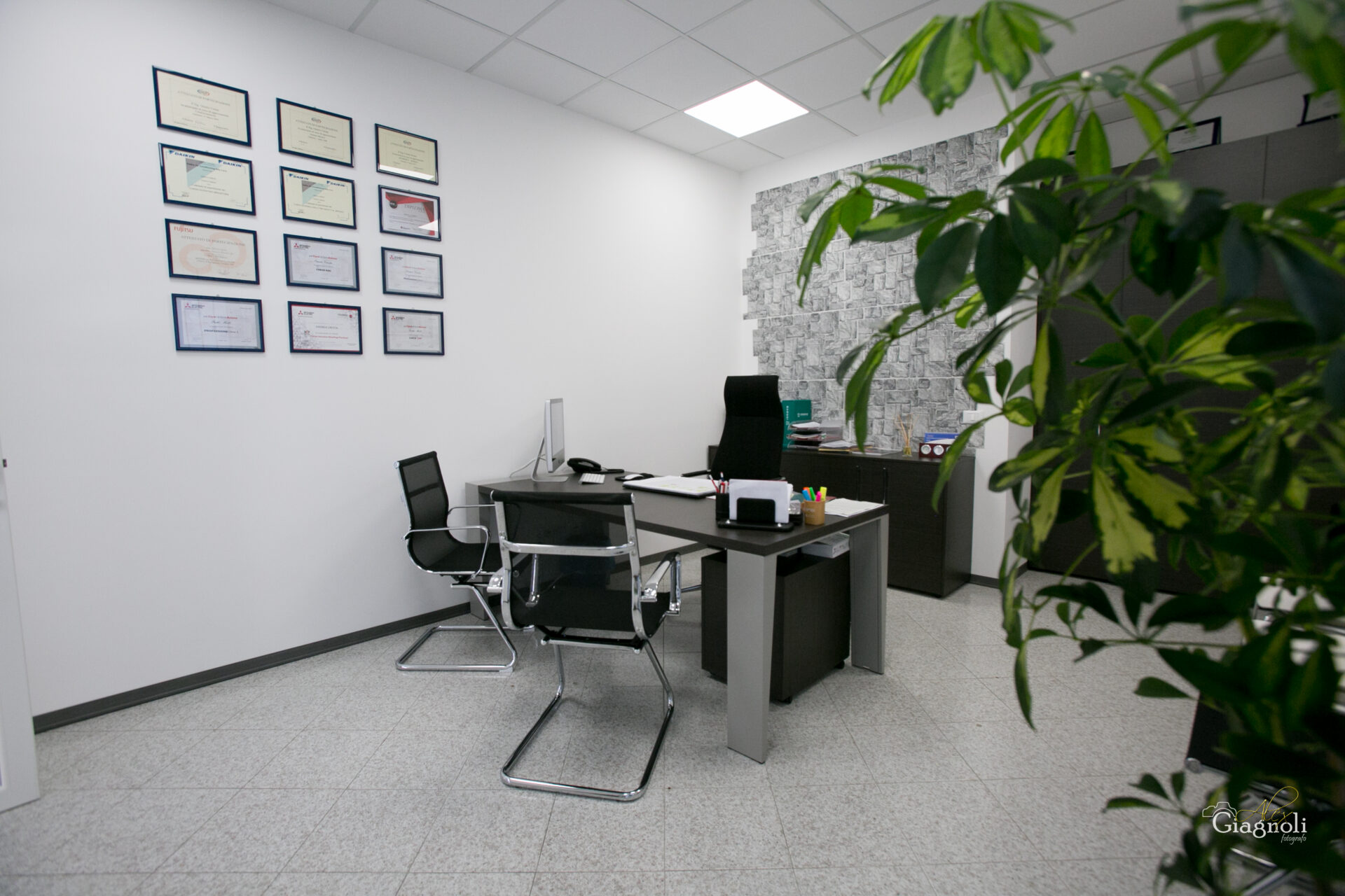Ufficio moderno con scrivania, sedie e diplomi appesi.