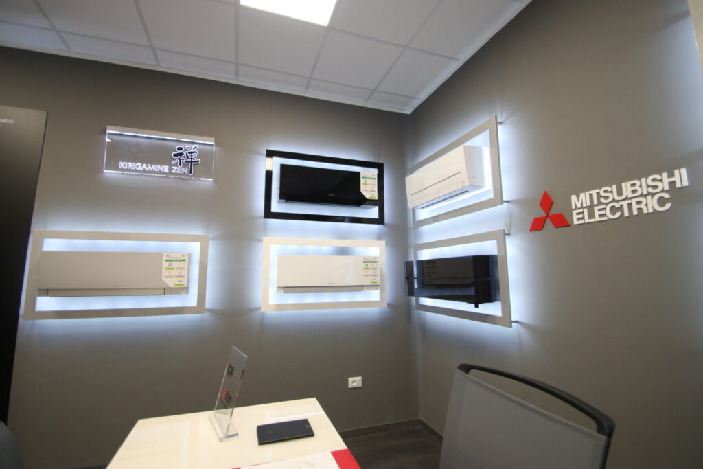 Esposizione di climatizzatori Mitsubishi Electric su parete grigia.