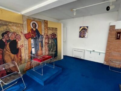 Stanza con affresco religioso e sedie trasparenti.