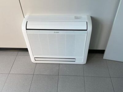 Condizionatore bianco montato a parete su pavimento piastrellato.