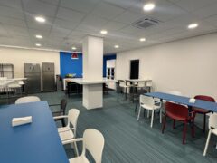 Sala mensa moderna con tavoli blu e sedie bianche.