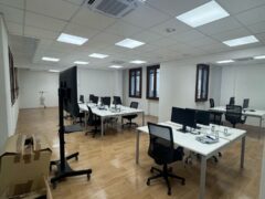 Ufficio moderno con scrivanie, sedie e computer.