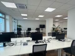 Ufficio moderno con scrivanie, sedie e computer.