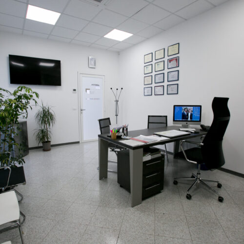 Ufficio moderno con scrivania, computer e diplomi alle pareti.
