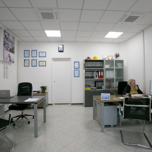 Ufficio moderno con scrivanie, sedie e scaffali.