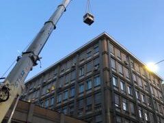 Gru solleva oggetto davanti a edificio alto.