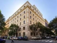 Edificio angolare con alberi e auto parcheggiate.