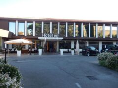 Facciata di un hotel con parcheggio e ombrelloni.