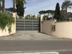 Cancello chiuso con muro e vegetazione circostante.