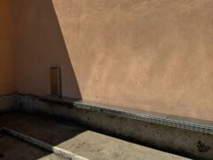Muro arancione con ombra triangolare e pavimento in cemento.